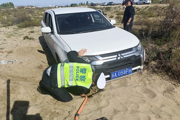 哈巴河县公安局交警大队执勤人员将车辆拖车绳挂在陷入沙地的车上